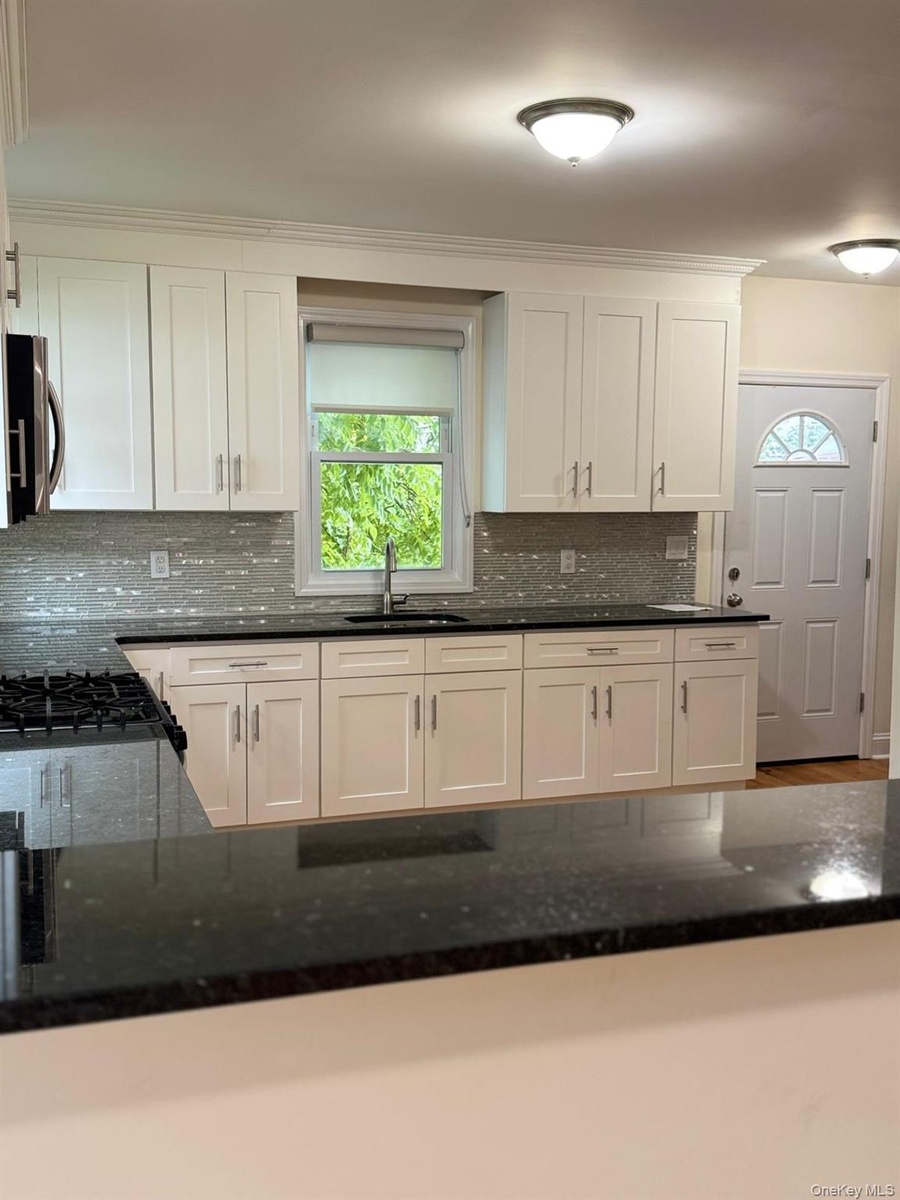 White shaker-style cabinetry with dark countertops, a tile backsplash, and stainless steel hardware