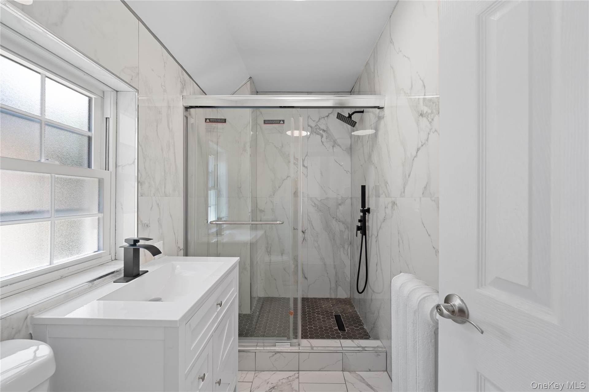 white vanity with integrated rectangular sink and matte black faucet, glass-enclosed shower, matte black shower fixtures, and white marble-look wall t