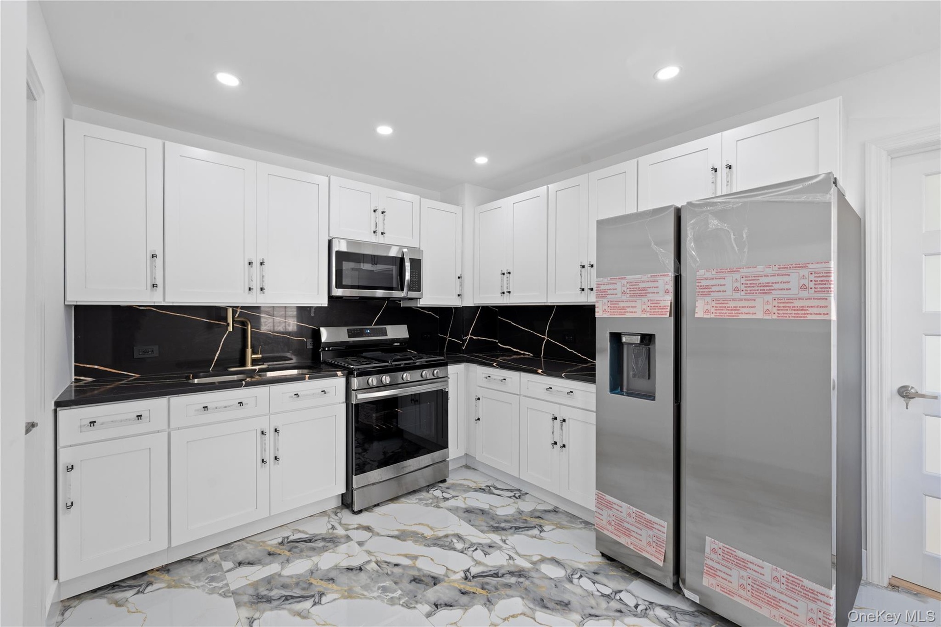 White cabinetry, black countertops with white veining, stainless steel appliances, and recessed lighting