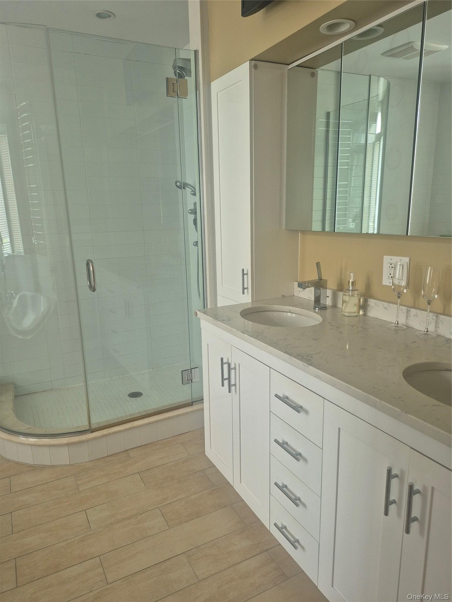 Master Bathroom with double vanity with integrated sinks, white cabinetry and light-toned countertop, mirrored medicine cabinet and stand-alone glass 