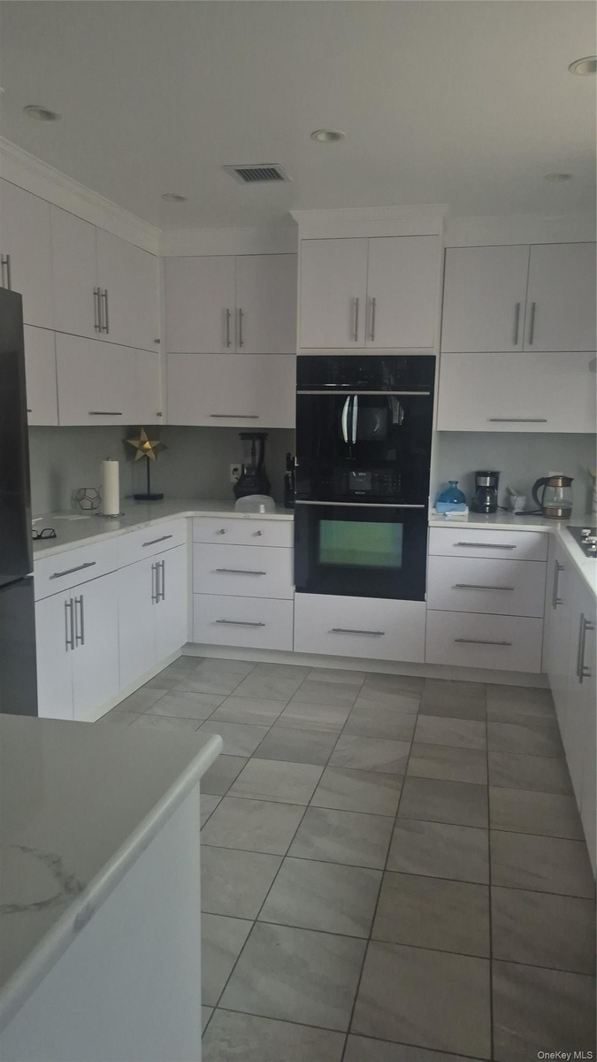 White cabinetry, stone-finish countertops, tile flooring, built-in wall oven, and built-in microwave and dishwasher