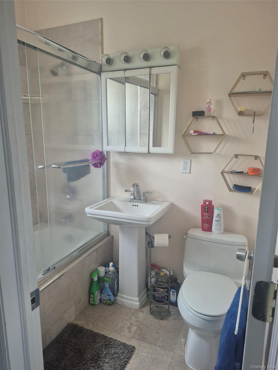 Pedestal sink with chrome faucet, wall-mounted medicine cabinet with integrated lighting, tiled shower surround with glass enclosure, wall-mounted hex