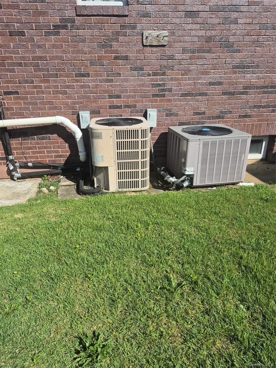 Brick exterior with two HVAC units and a ground-level window and landscaped yard area
