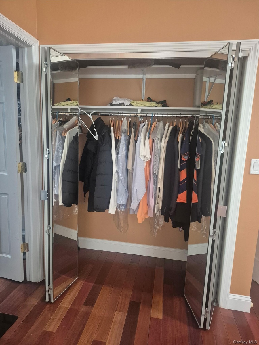 Additional mirrored closet in Master Bedroom with bi-fold doors, integrated upper shelving, and wood-finish flooring