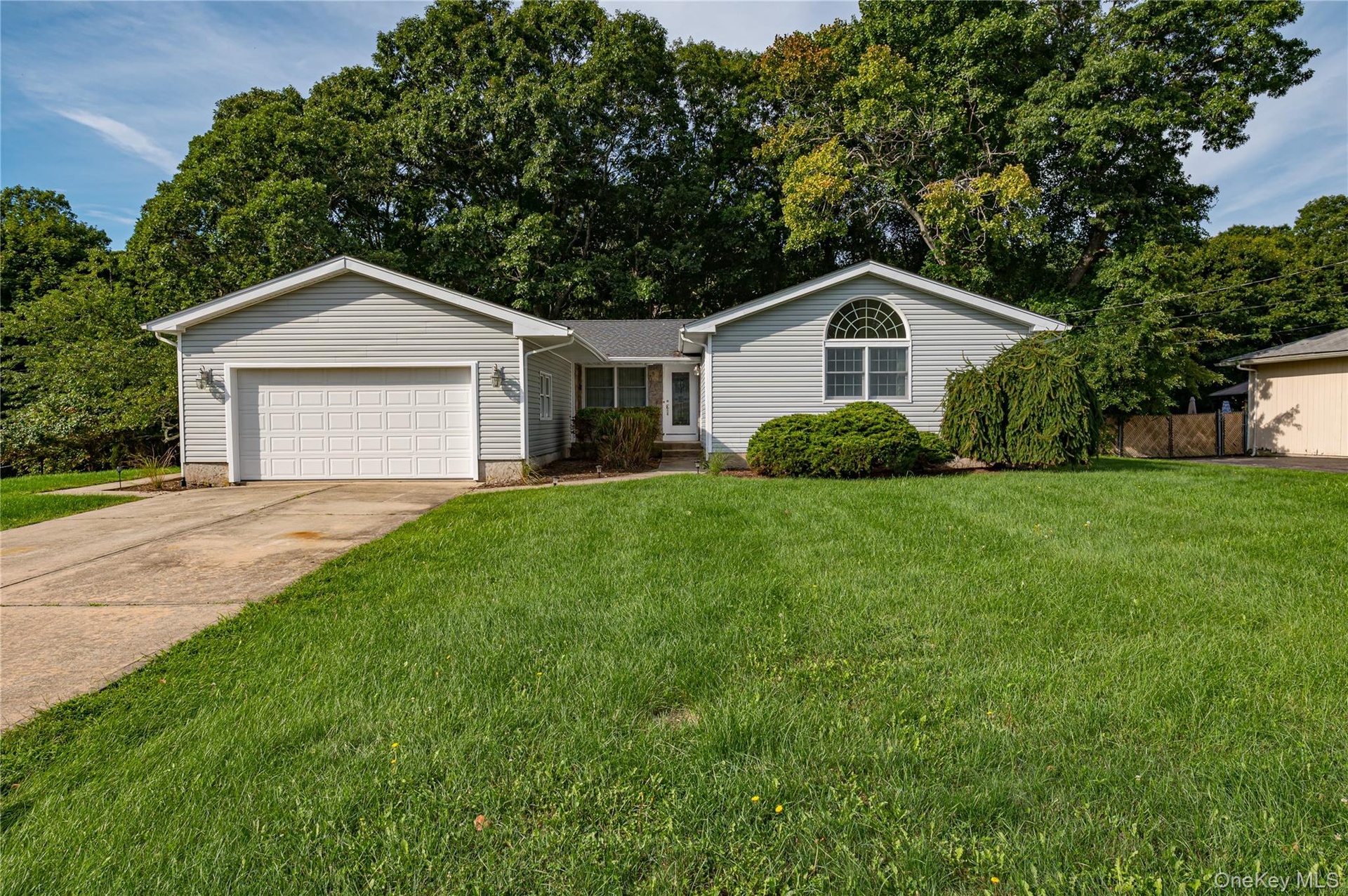Grey vinyl siding exterior with a concrete driveway, attached garage, and a semicircular arched window