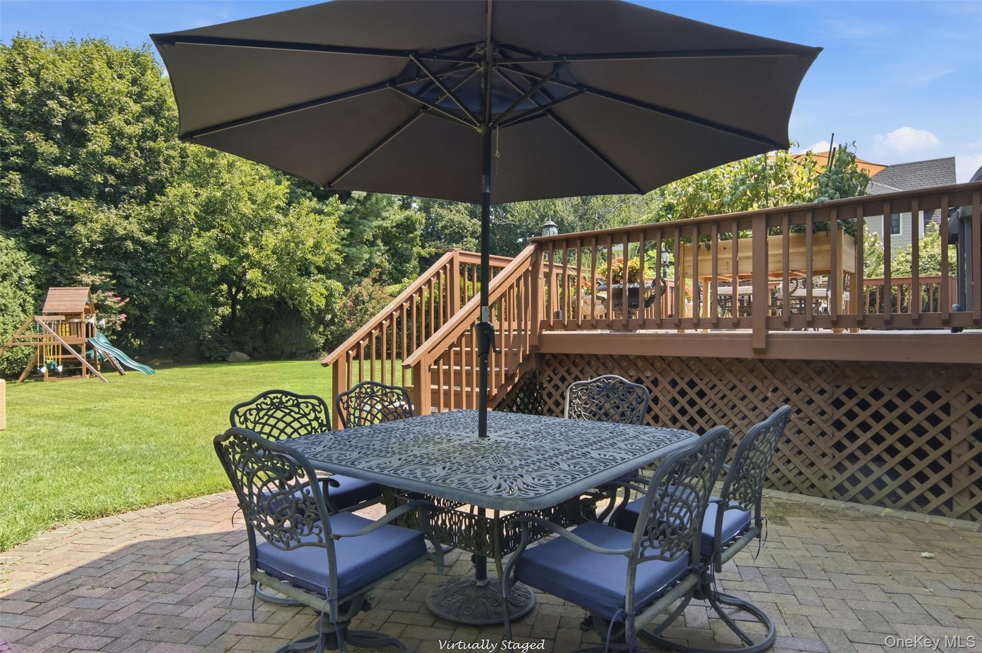 Brick paver patio with a wood deck, wood railings, and lattice skirting, featuring a spacious grass yard