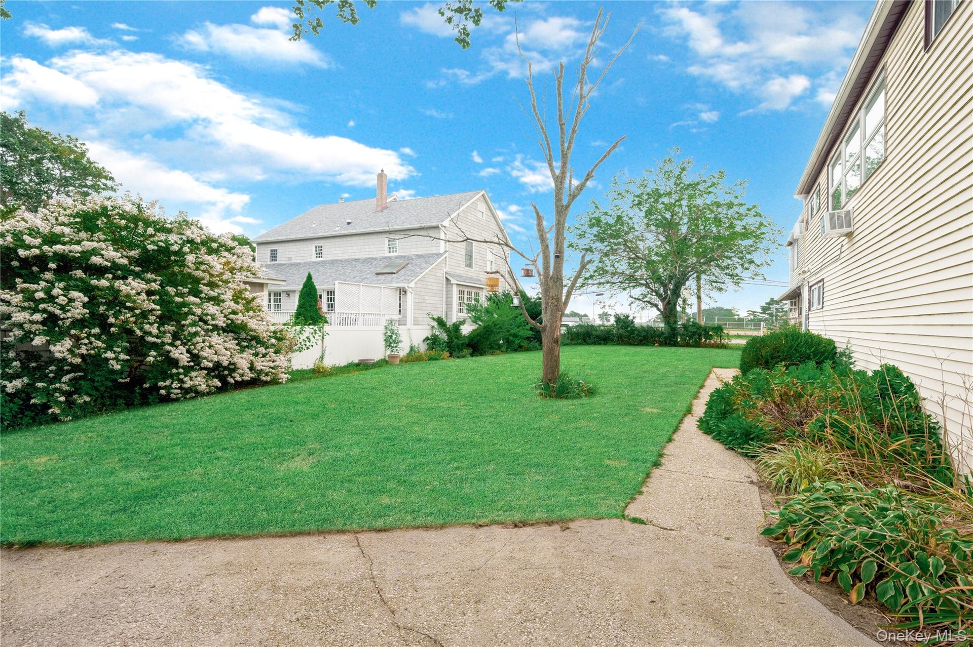Expansive lawn, mature landscaping, paved pathway, and a privacy fence
