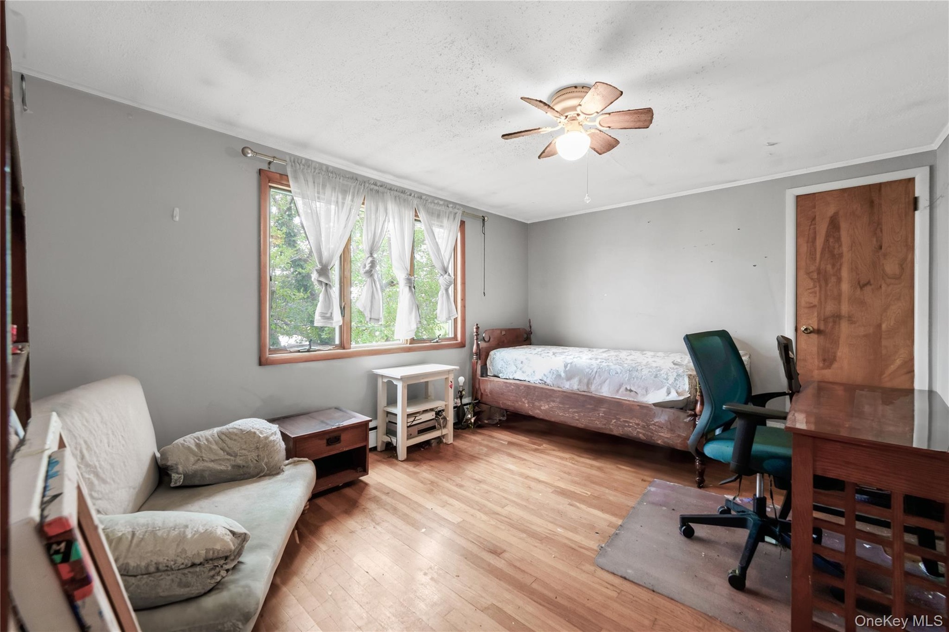 Wood-finish flooring, a ceiling fan with light fixture, and a window with wood trim