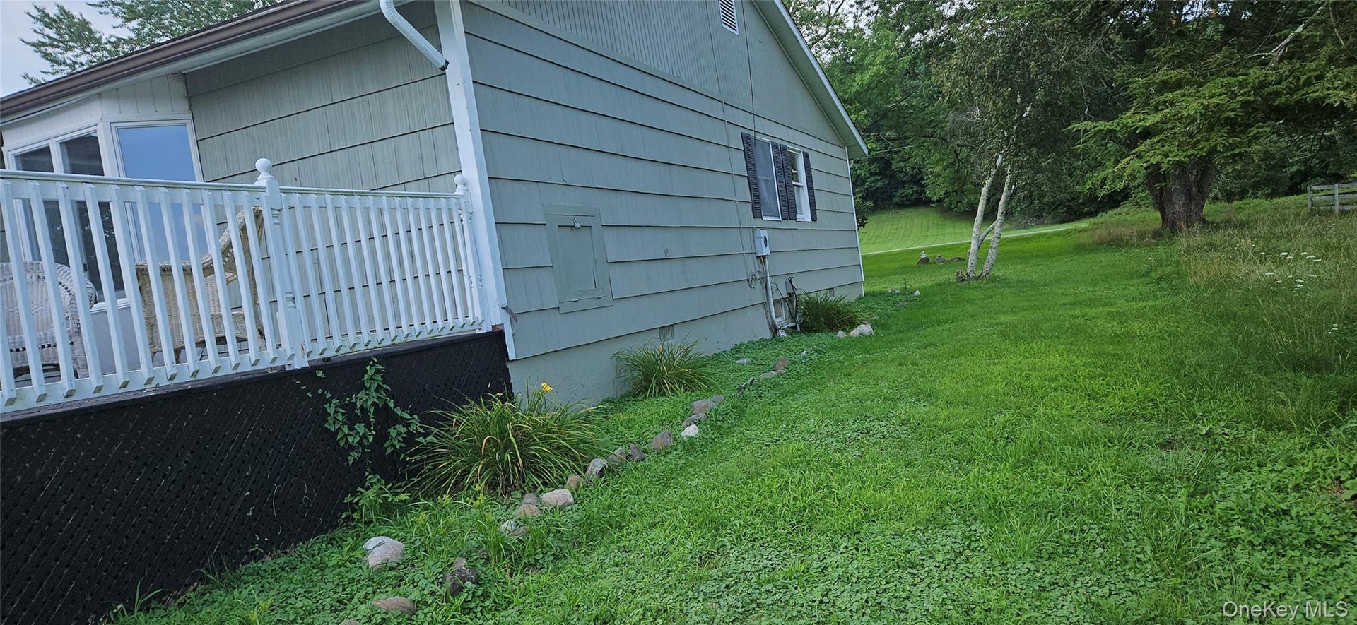 Exterior siding with window, white deck railing, and sloped grassy area