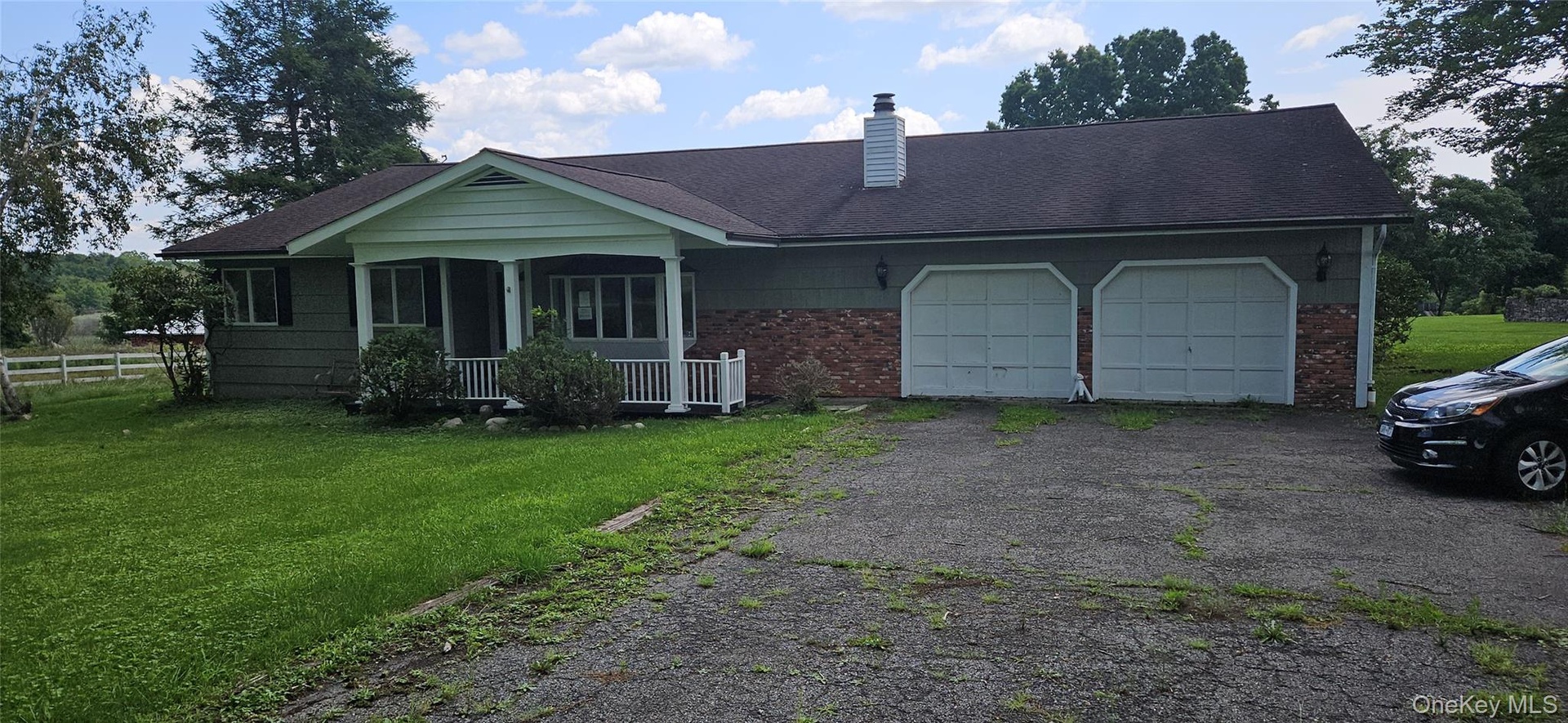 Single-story residence featuring a covered front porch with white railing, a two-car garage, brick accents, and a driveway