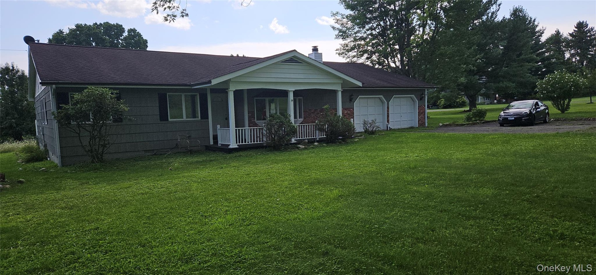 Ranch-style residence featuring a covered front porch with white railings, a two-car garage, and a charcoal shingle roof