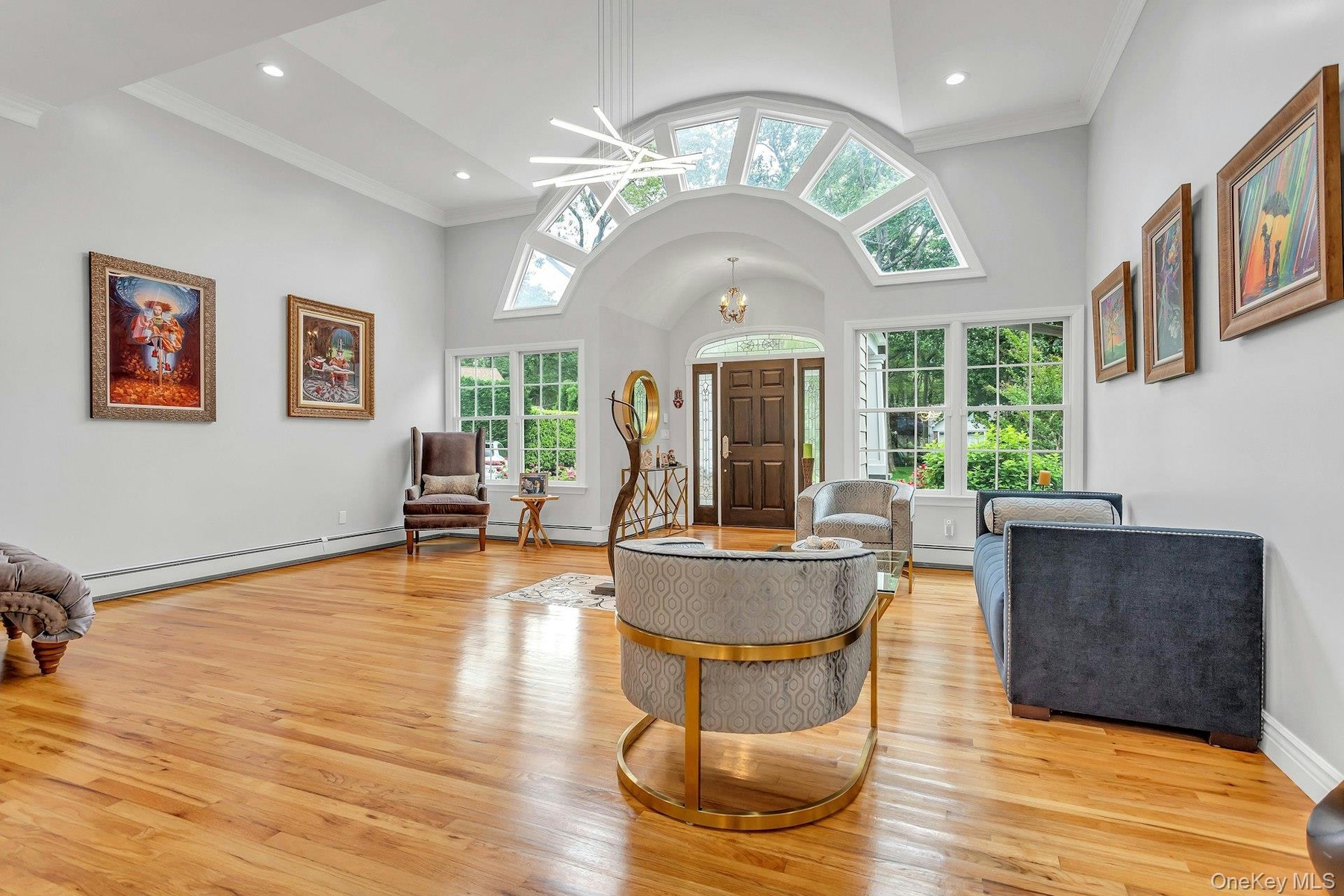 Entryway featuring light wood finished floors, baseboard heating, ornamental molding, a chandelier, and high vaulted ceiling