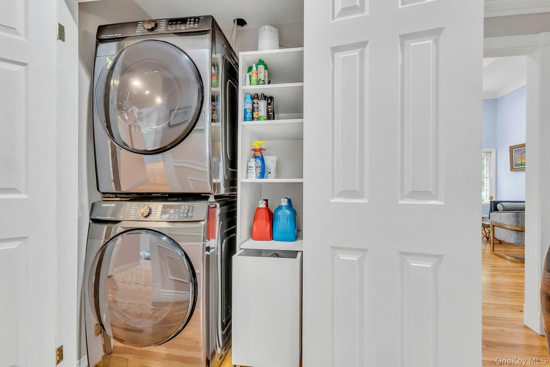 Laundry room with stacked washer and clothes dryer, wood finished floors, and crown molding