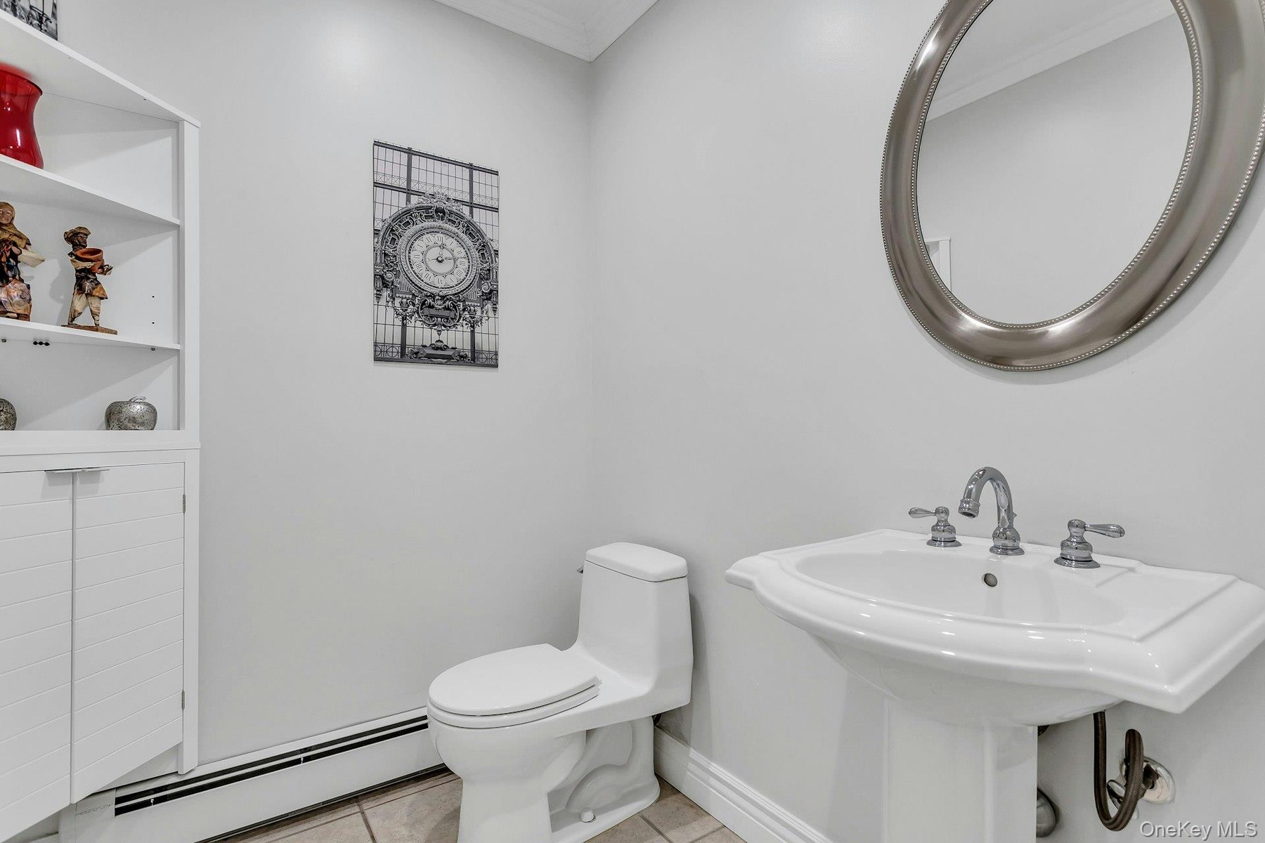 Half bath featuring a baseboard radiator, tile patterned flooring, crown molding, toilet, and a sink