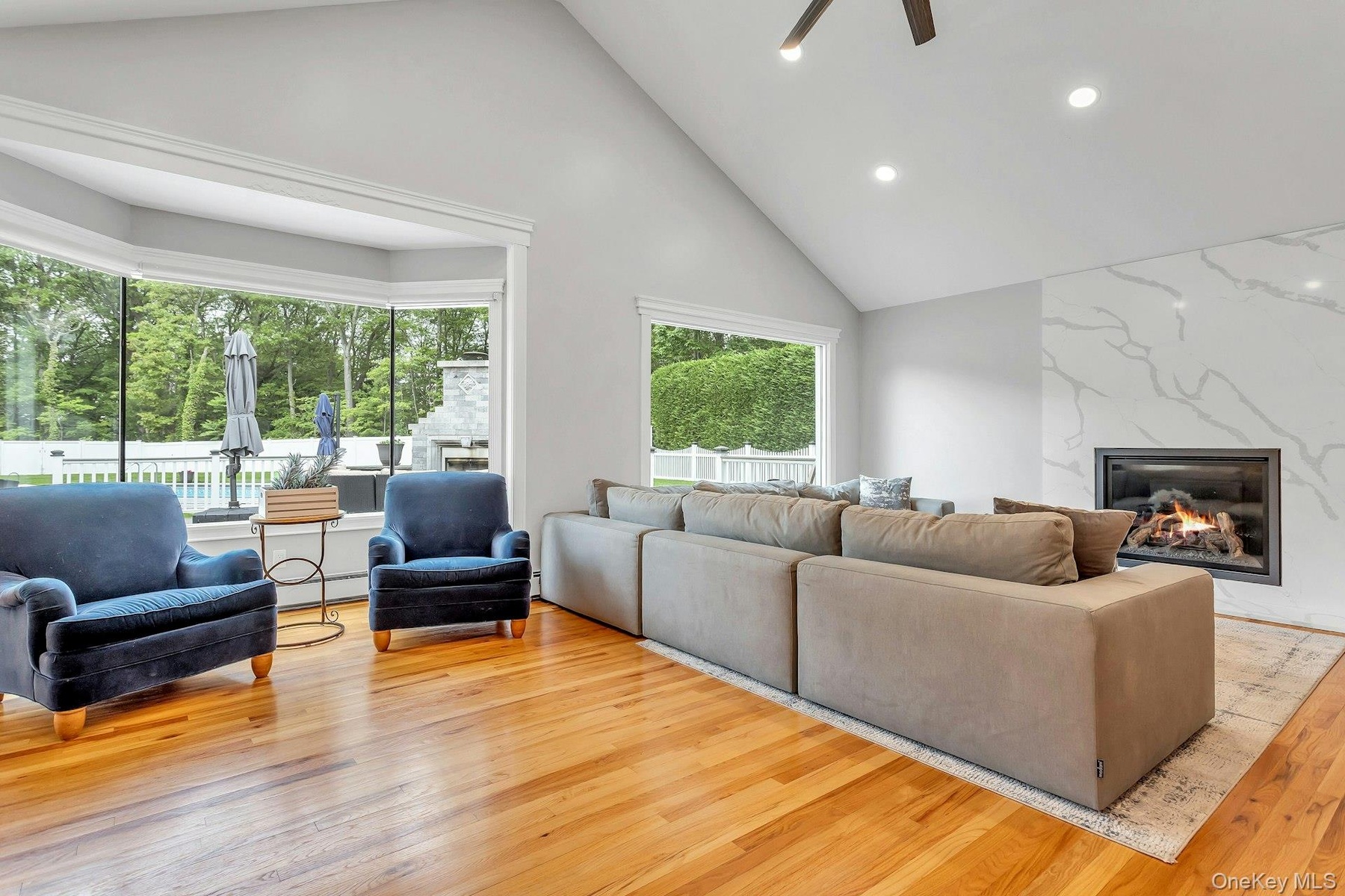 Living room featuring light wood-style floors, high vaulted ceiling, a fireplace, a ceiling fan, and recessed lighting