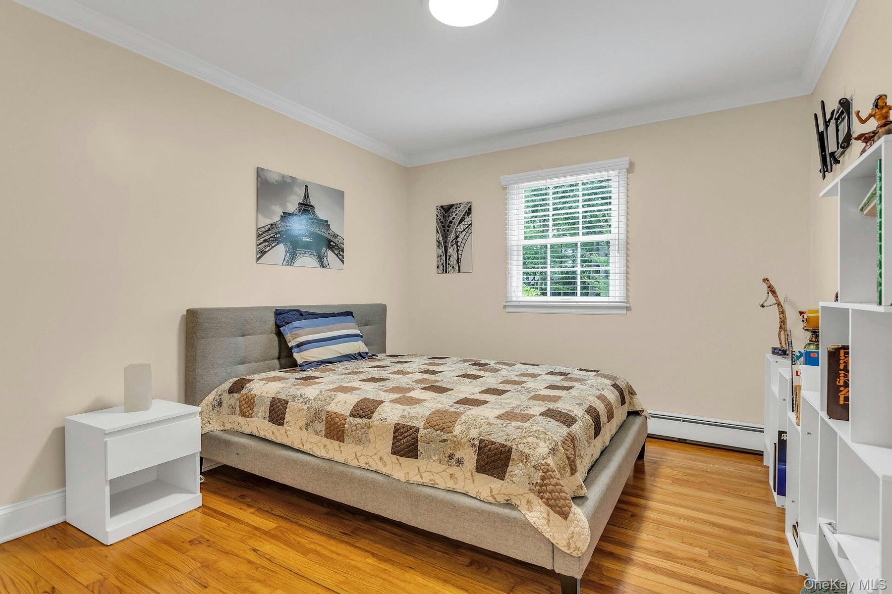 Bedroom with baseboard heating, ornamental molding, and light wood finished floors