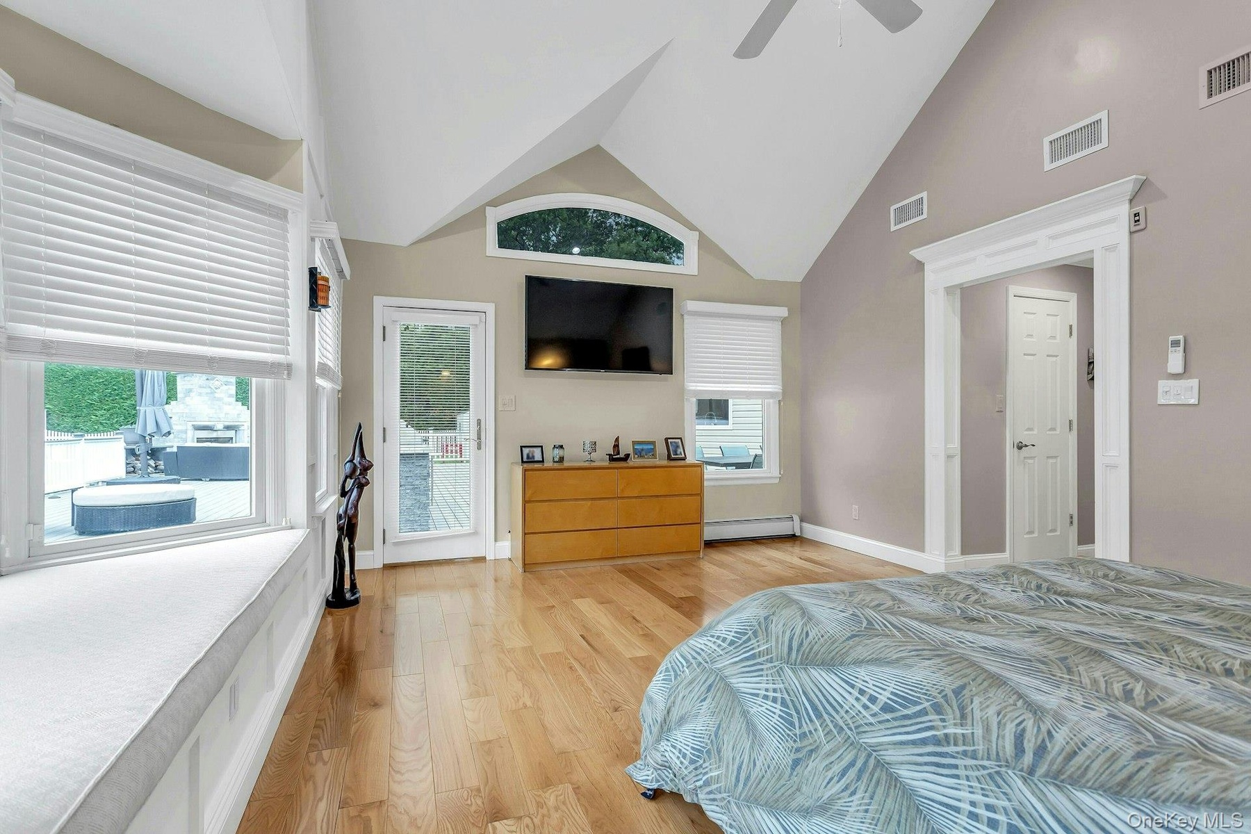 Bedroom with light wood-style flooring, a baseboard radiator, a ceiling fan, baseboards, and high vaulted ceiling