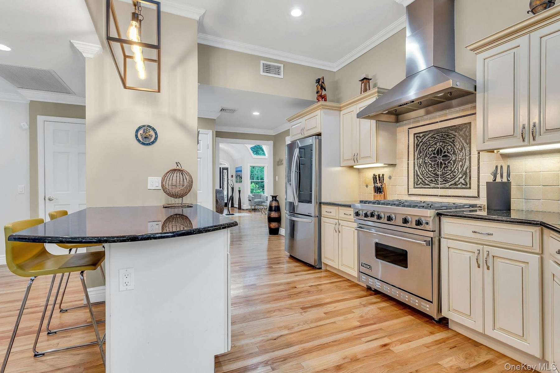 Kitchen with exhaust hood, stainless steel appliances, crown molding, cream cabinets, and a breakfast bar