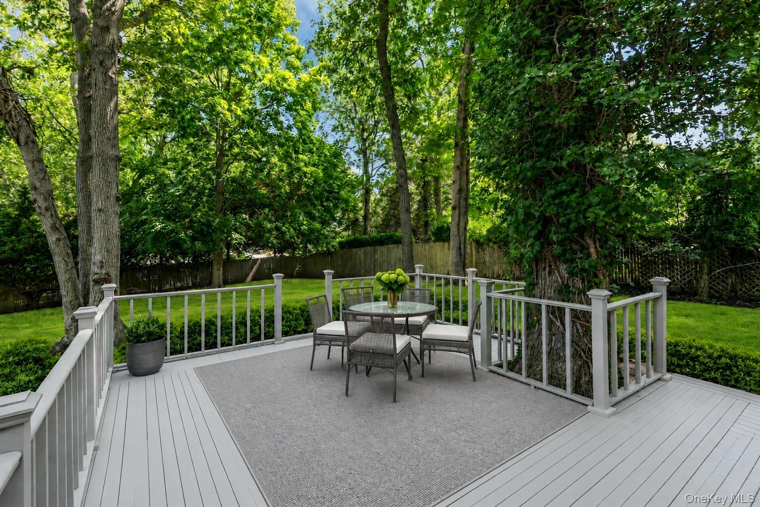 Expansive outdoor deck with light gray decking and white railing, surrounded by mature trees and manicured lawn