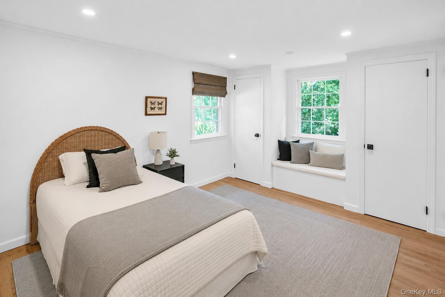 Recessed lighting, wood-finish flooring, two panel doors with black hardware, window with integrated seating, and a second window with a woven shade