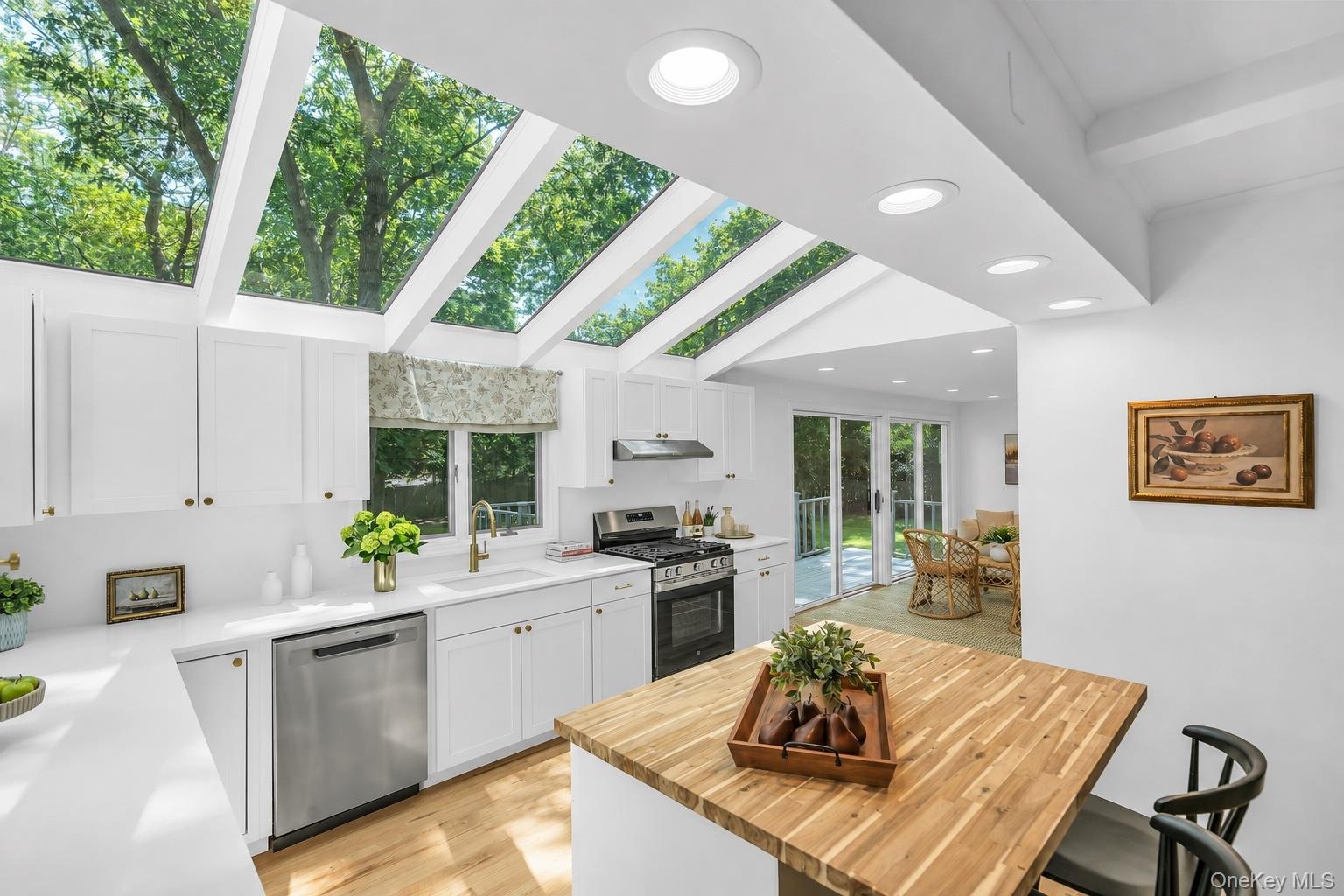 Kitchen with vaulted ceiling and integrated skylights, white cabinetry, stainless steel appliances, a wood-finish island, and recessed lighting