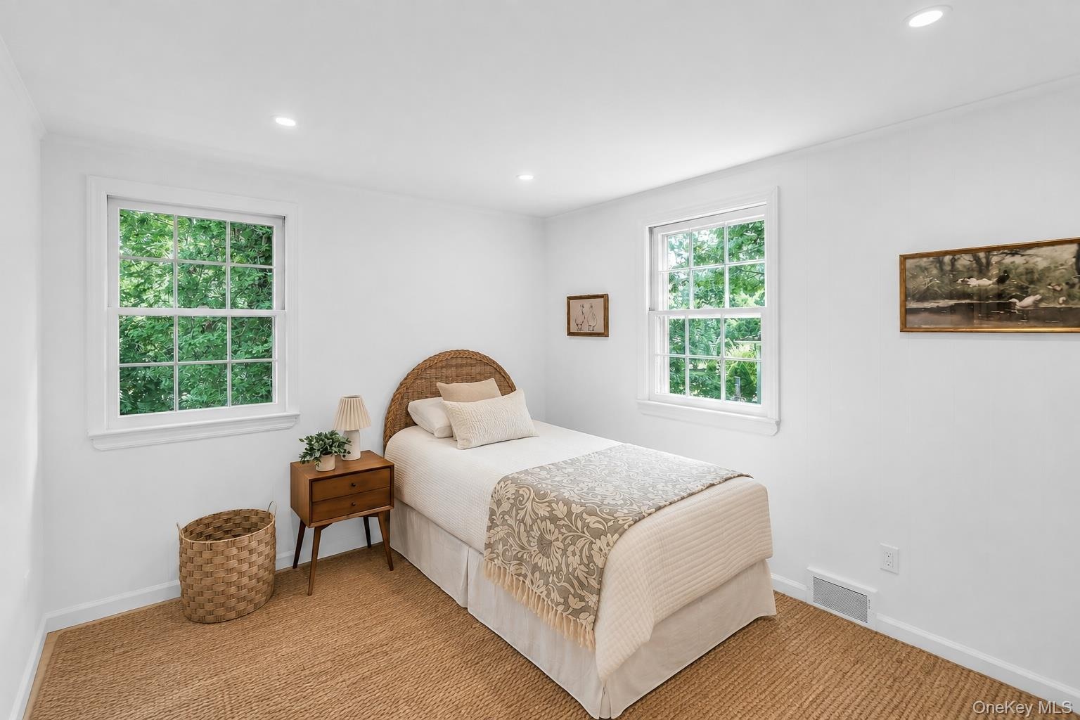 Recessed lighting illuminates a room with two large windows and a woven area rug