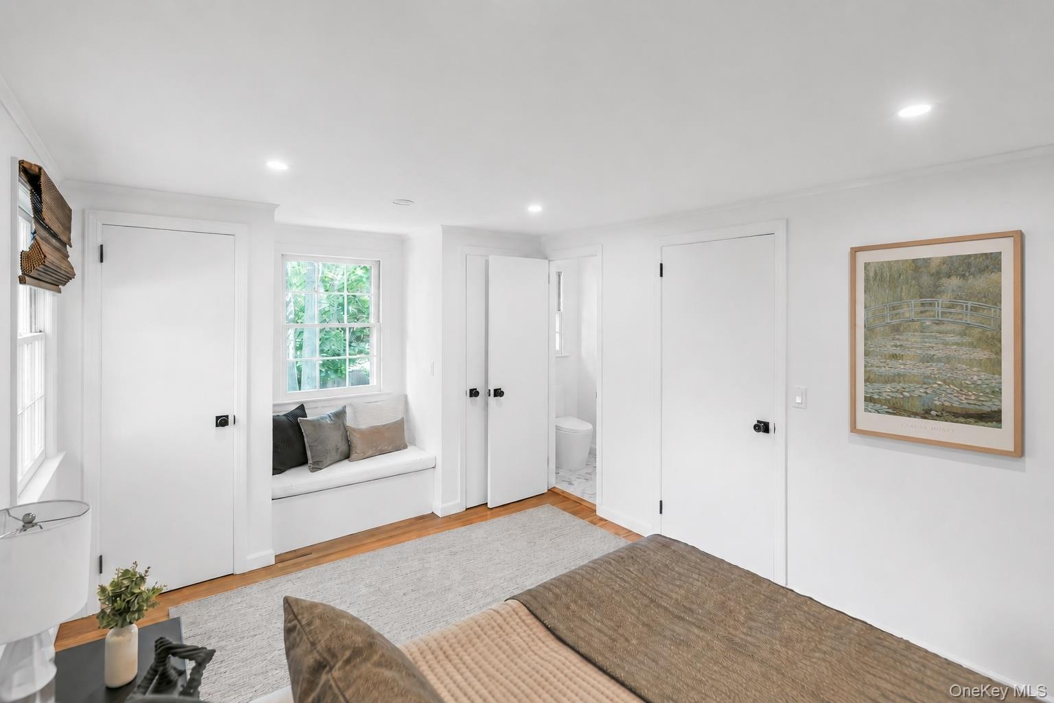 Window seat with integrated storage, wood-finish flooring, recessed lighting, white interior doors with dark hardware, and a window with natural light