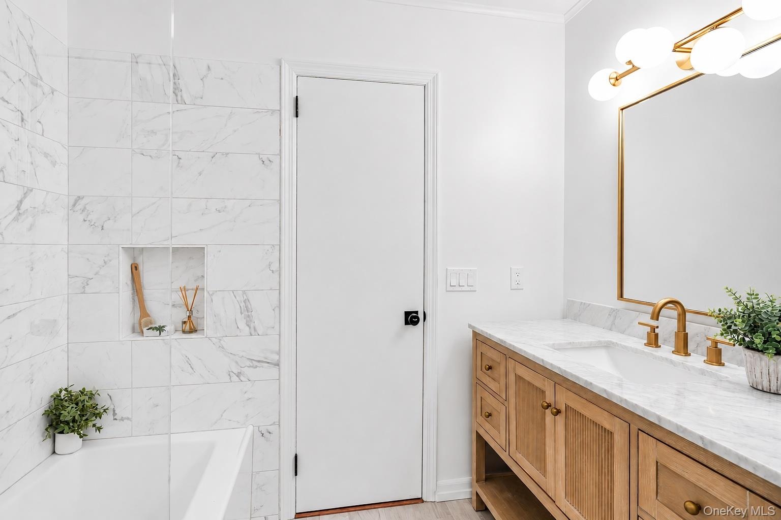 Bathroom featuring a natural wood-finish vanity with a white countertop, gold-toned faucet and cabinet hardware, and a framed mirror with a modern lig