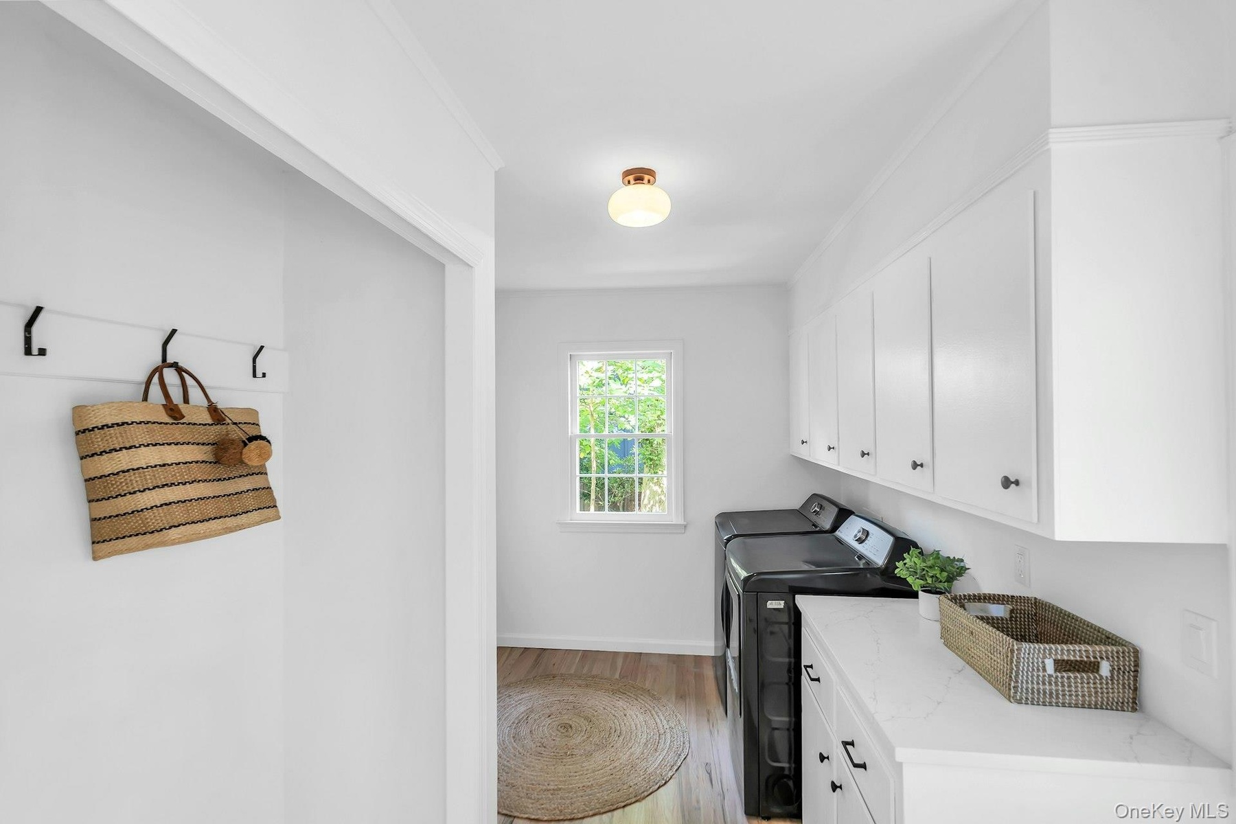 Laundry area featuring wood-finish flooring, white cabinetry, a built-in countertop, and a window
