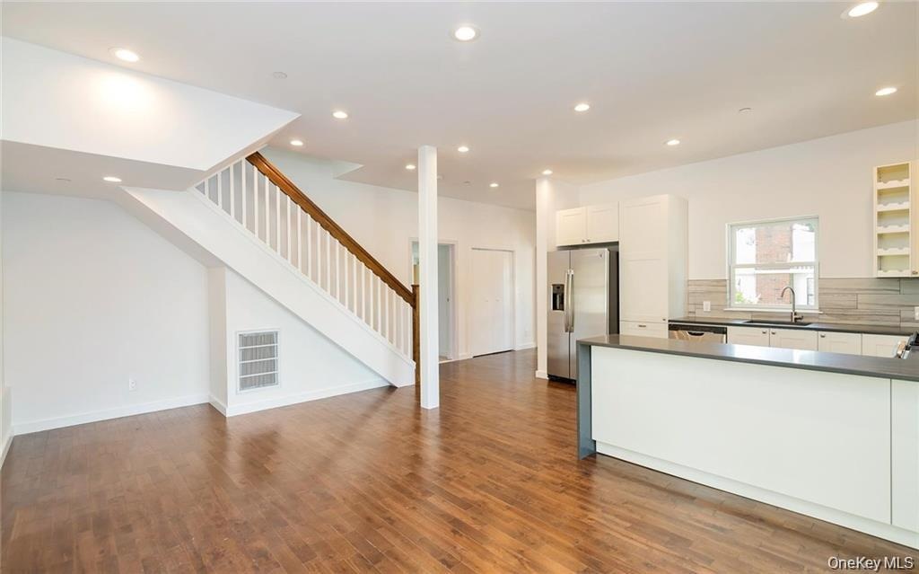 Kitchen with open floor plan, white cabinetry, stainless steel refrigerator with ice dispenser, dark countertops, and backsplash