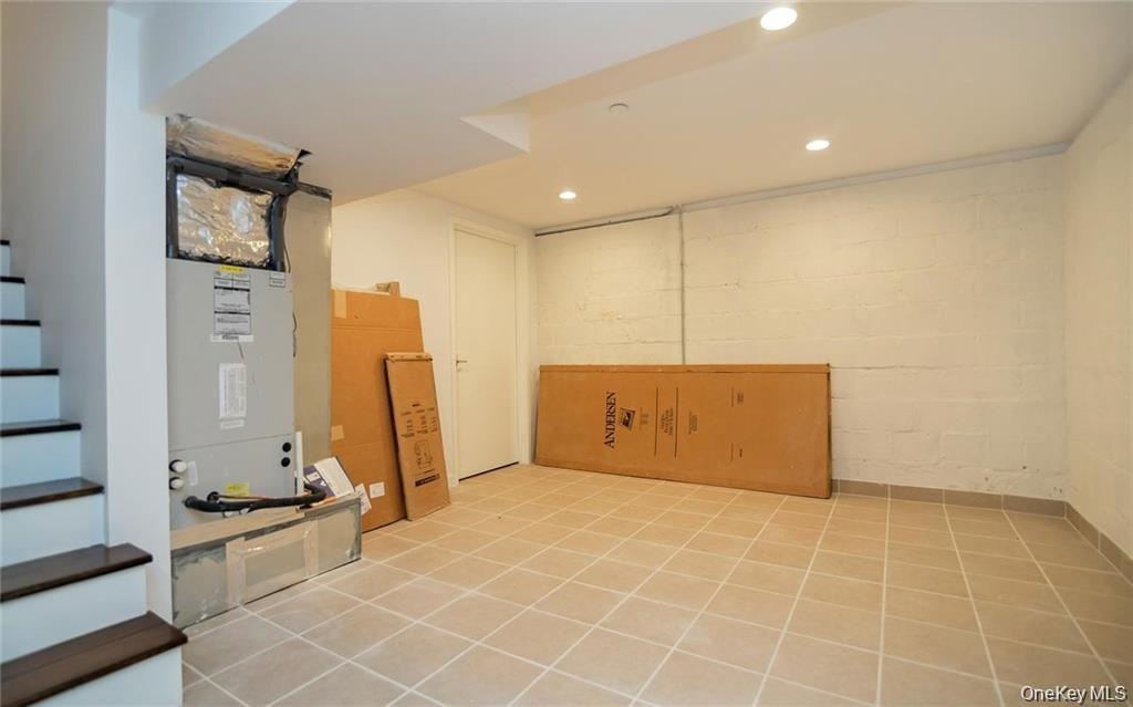 Finished basement featuring stairway, recessed lighting, light tile patterned flooring, concrete block wall, and heating unit