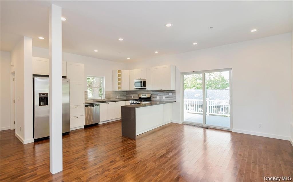 Kitchen featuring stainless steel appliances, dark countertops, white cabinets, open floor plan, and tasteful backsplash