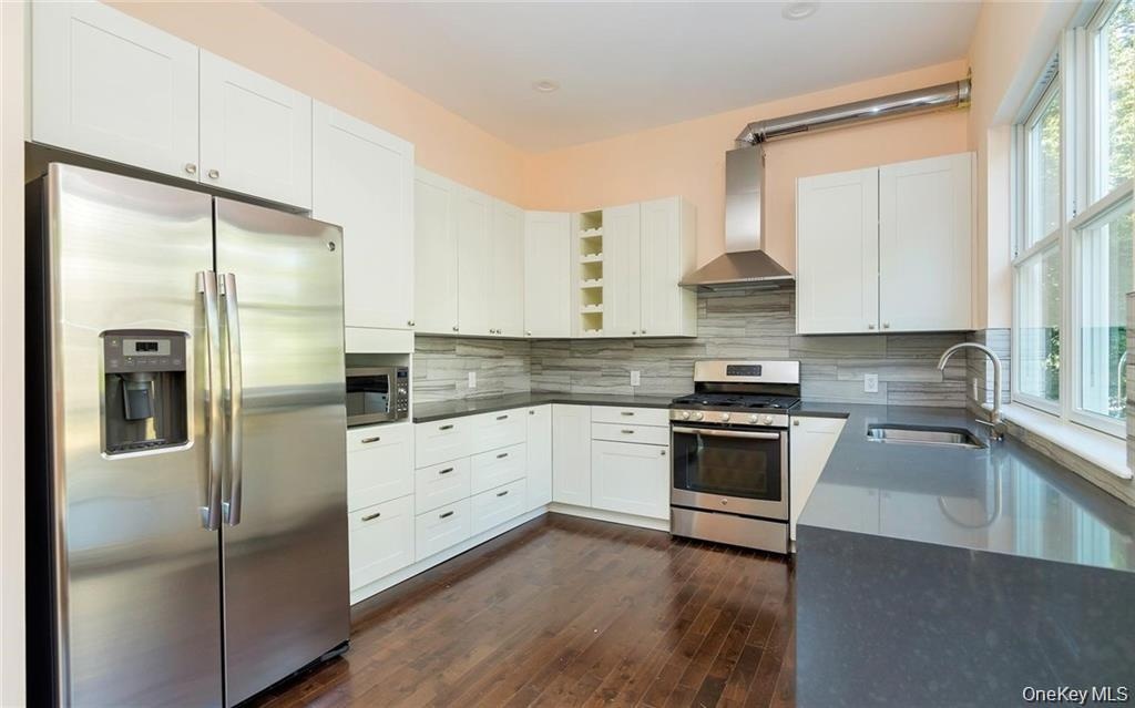 Kitchen featuring stainless steel appliances, open shelves, white cabinetry, wall chimney range hood, and backsplash