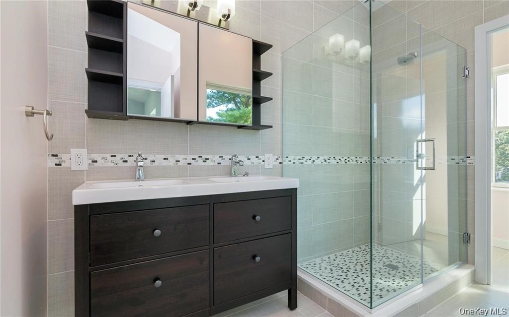 Full bathroom with tile walls, double vanity, a stall shower, decorative backsplash, and light tile patterned floors