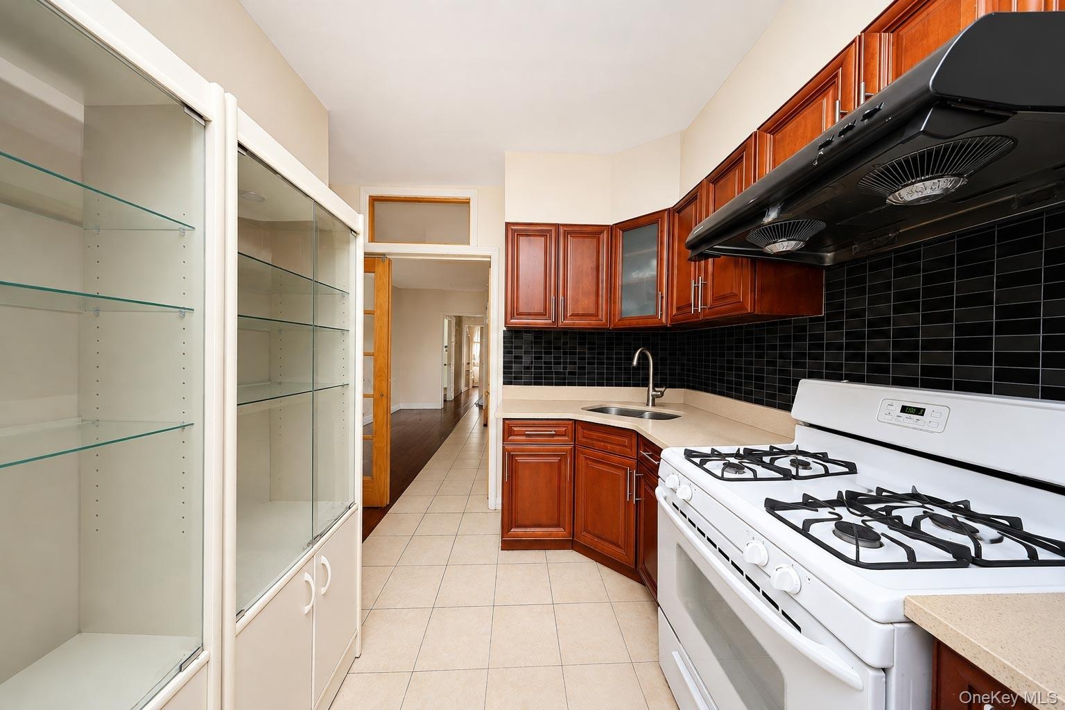 Kitchen featuring wood cabinetry, a black tile backsplash, light-colored countertops, and a white gas range