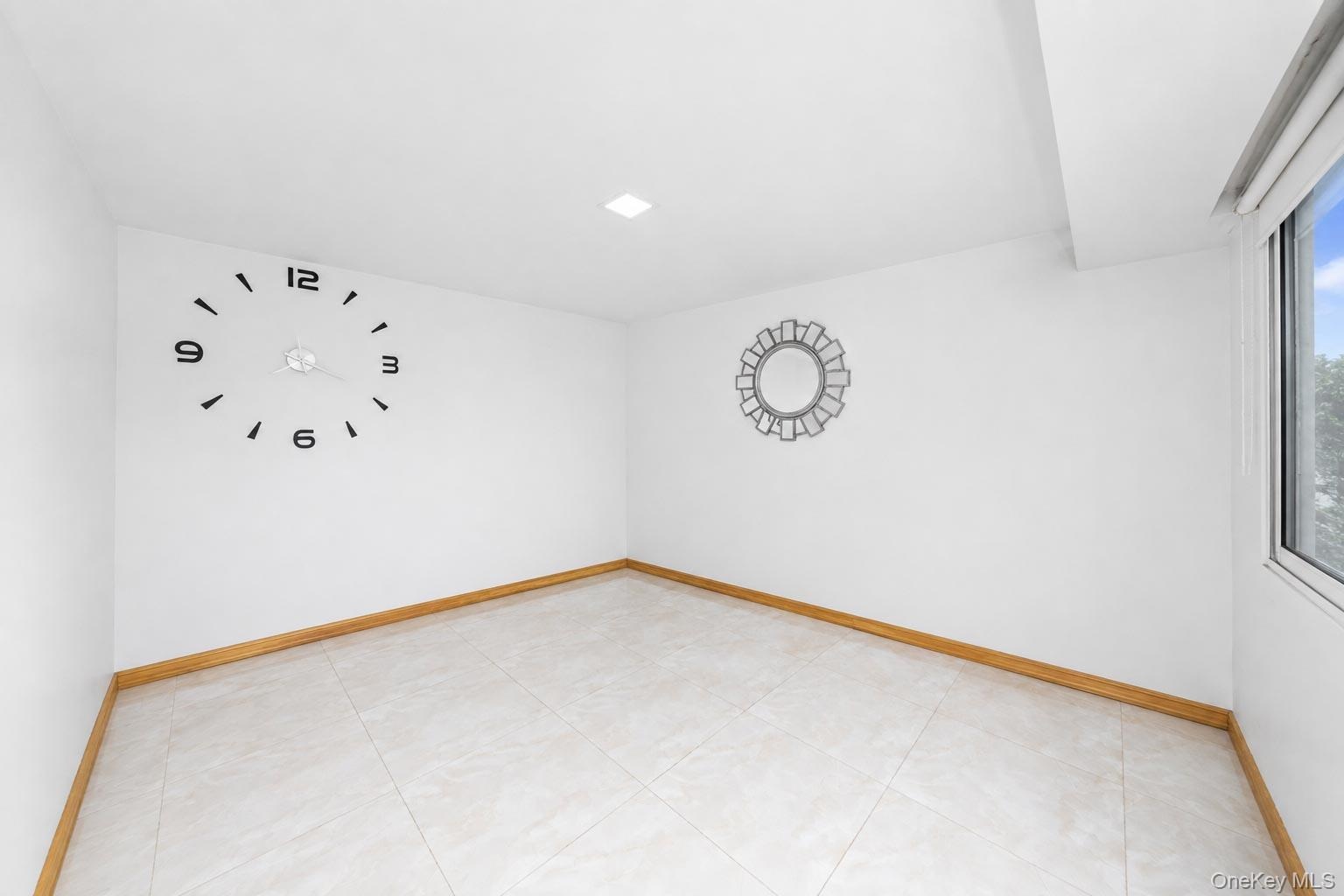 Recessed ceiling lighting, light-toned tile flooring, light wood-finish baseboards, and a window with a white frame