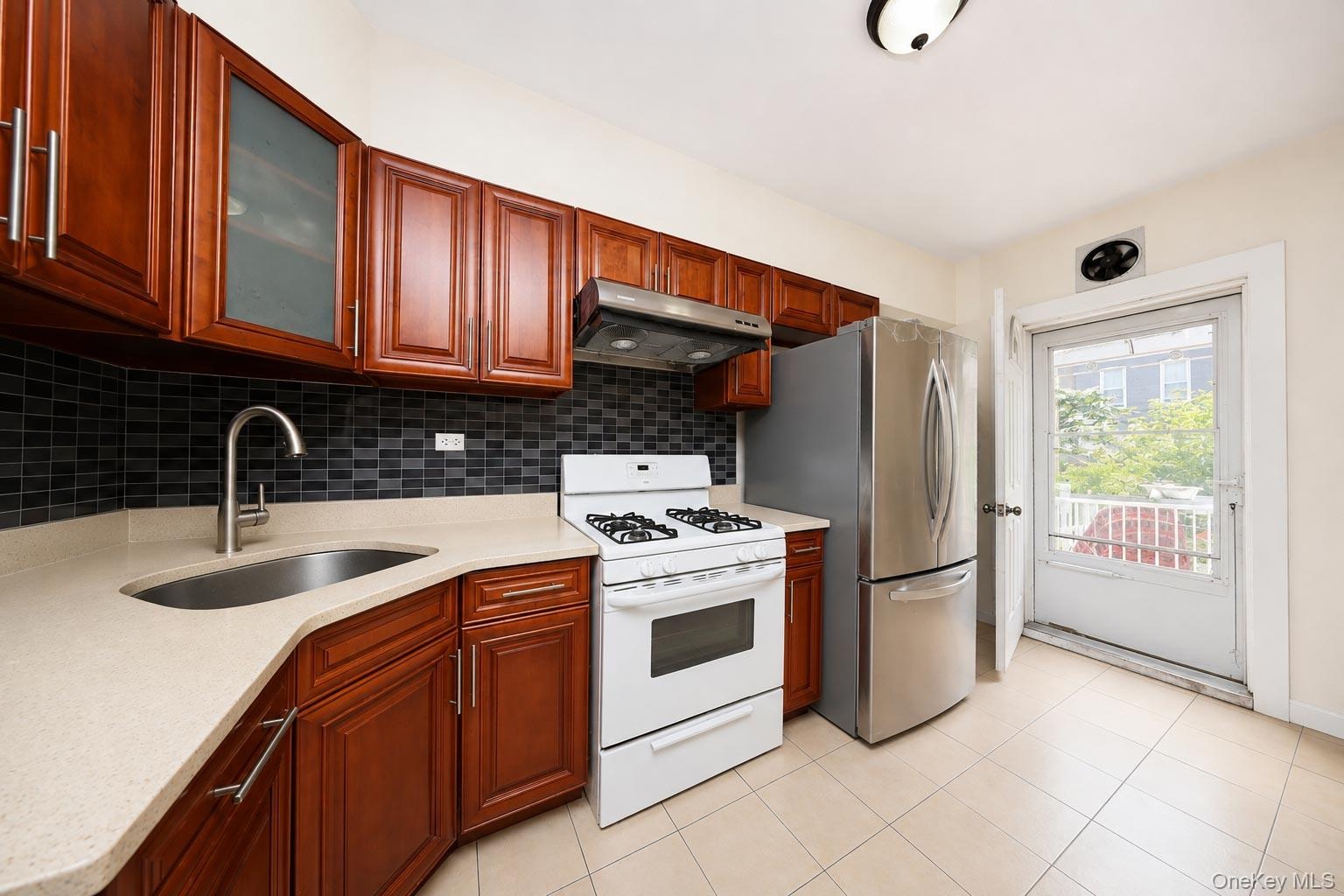 Kitchen featuring wood-finish cabinetry, light-toned countertops, a stainless steel sink with a gooseneck faucet, a tile backsplash, and a stainless s