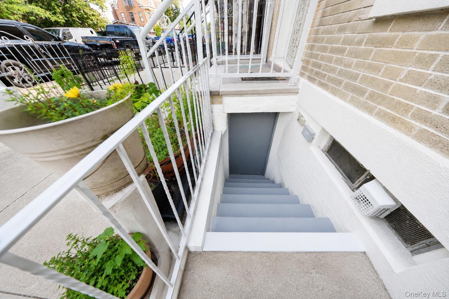 Ground-level entry with concrete stairs and white metal railings, beige brick exterior, and a small window unit