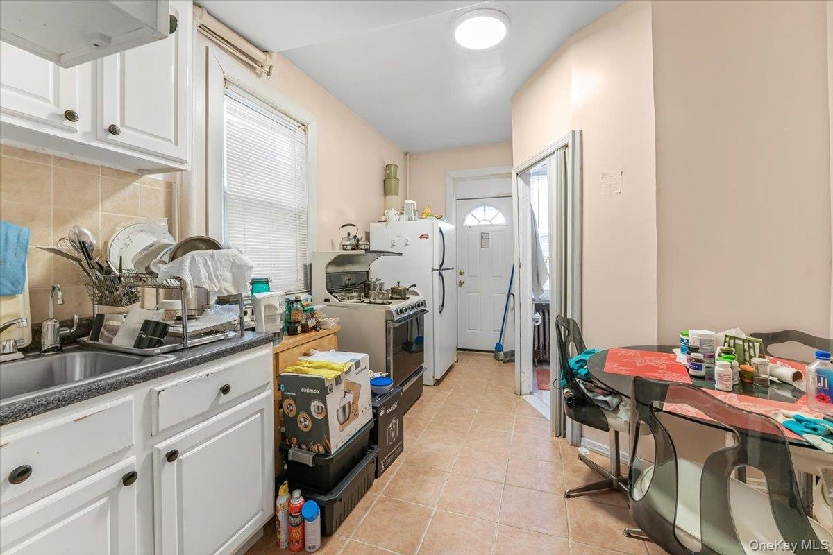 Kitchen with light tile patterned floors, tasteful backsplash, dark countertops, white cabinets, and white appliances