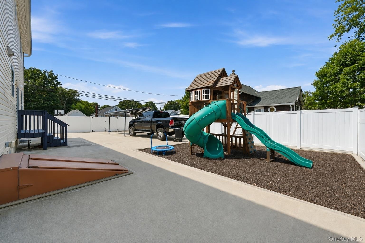 Spacious concrete patio with a separate mulched play area, a privacy fence, and an exterior basement entry