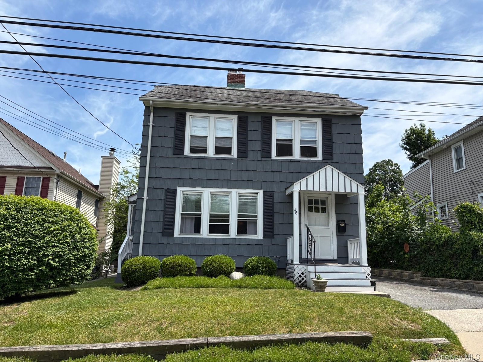 Two-story residence featuring shingle siding, a front porch with an awning, and a manicured lawn