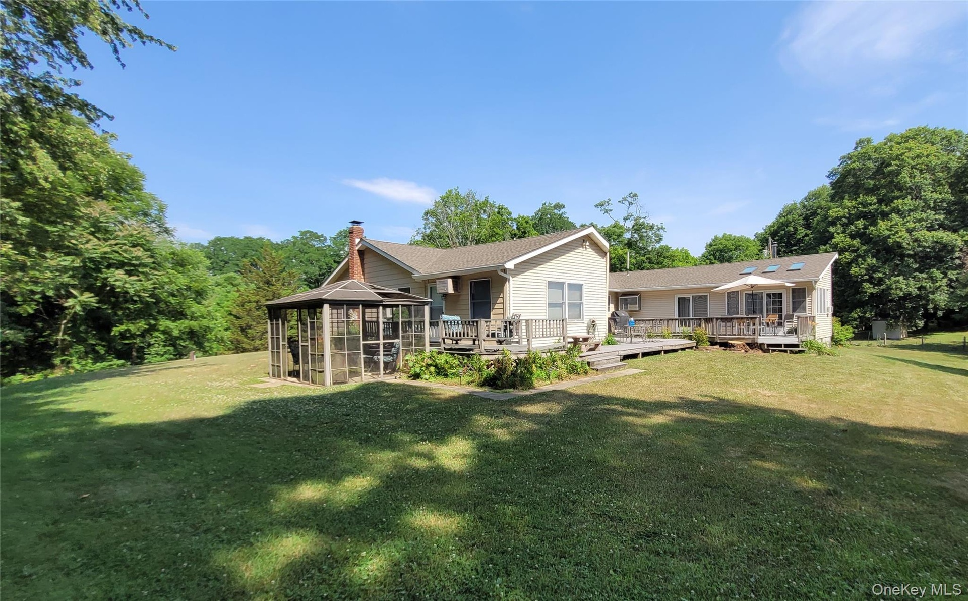 Expansive grassy yard with mature trees, a multi-level wood deck, and a screened outdoor structure on the side of the four-bedroom unit