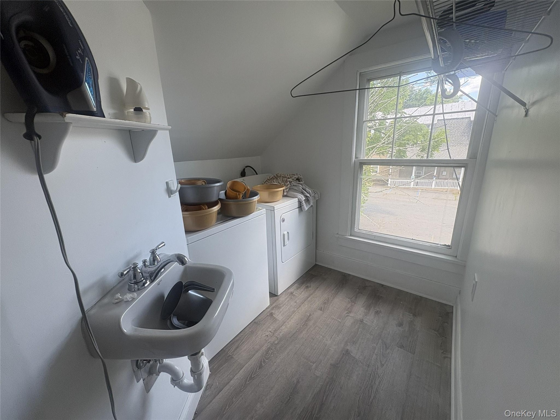 Wall-mounted utility sink, white shelving, wood-finish flooring, and a single window