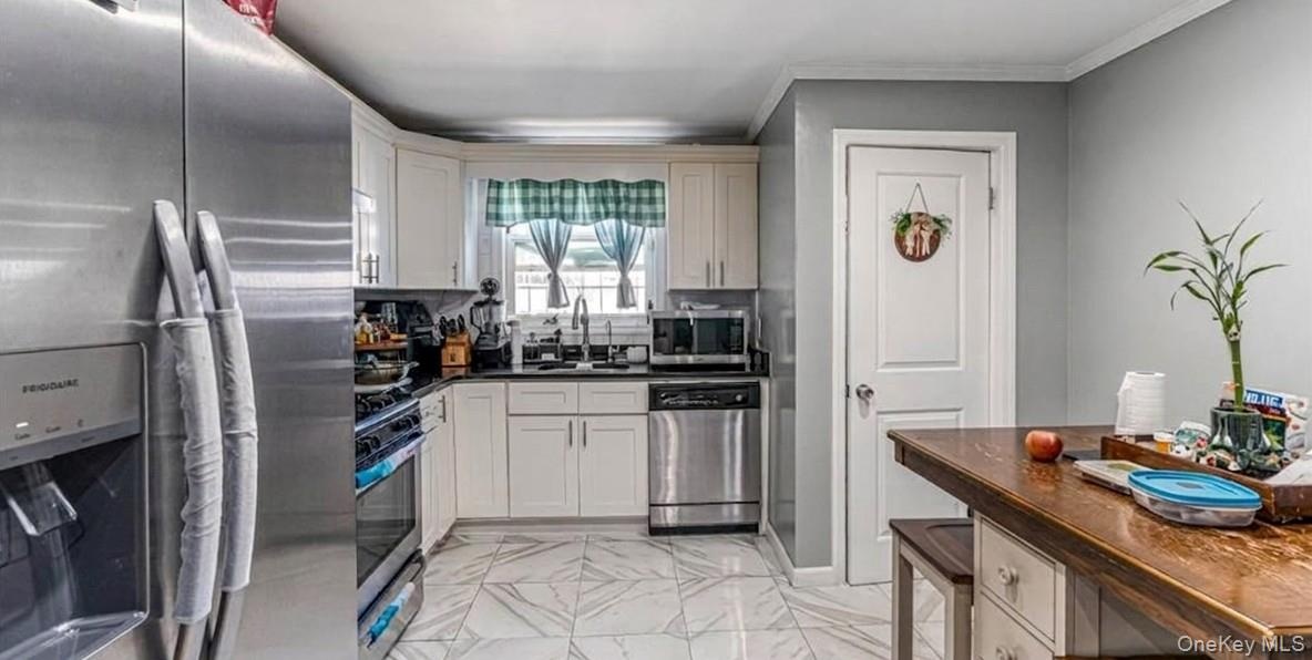The first-floor kitchen features an open layout with bright marble-look flooring, crisp white cabinetry, and modern stainless steel appliances. A larg