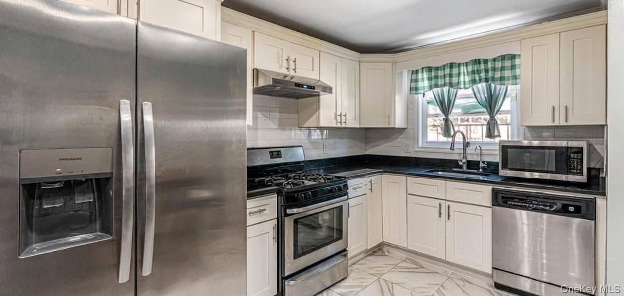 The first-floor kitchen features an open layout with bright marble-look flooring, crisp white cabinetry, and modern stainless steel appliances. A larg