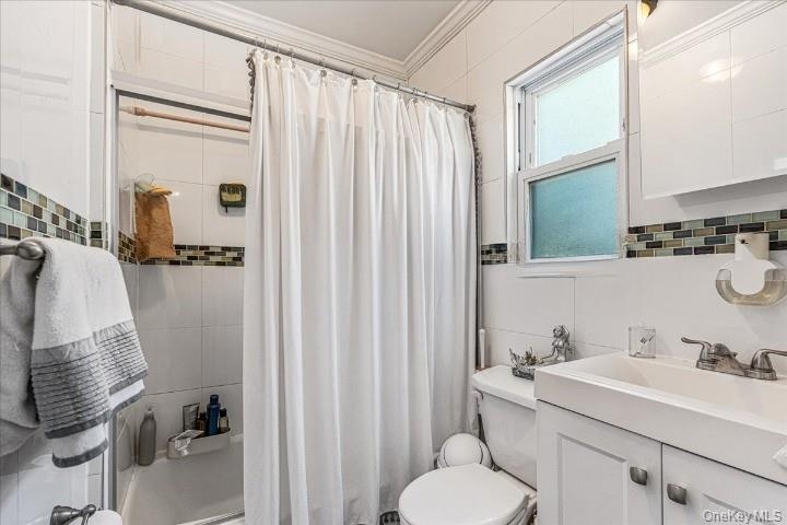 The second floor bathroom is clean and bright, featuring a white vanity, matching wall tiles, and a stylish mosaic border. A frosted window lets in gr