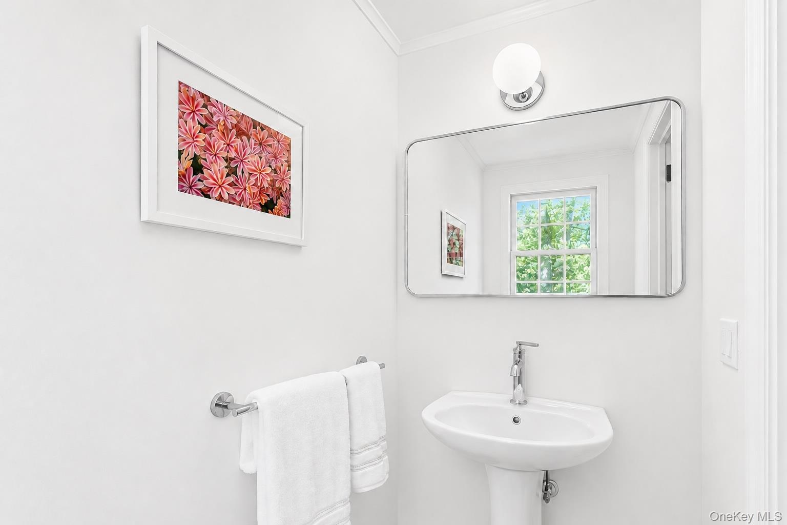 Pedestal sink with chrome faucet, wall-mounted mirror with rounded corners, and a chrome towel bar