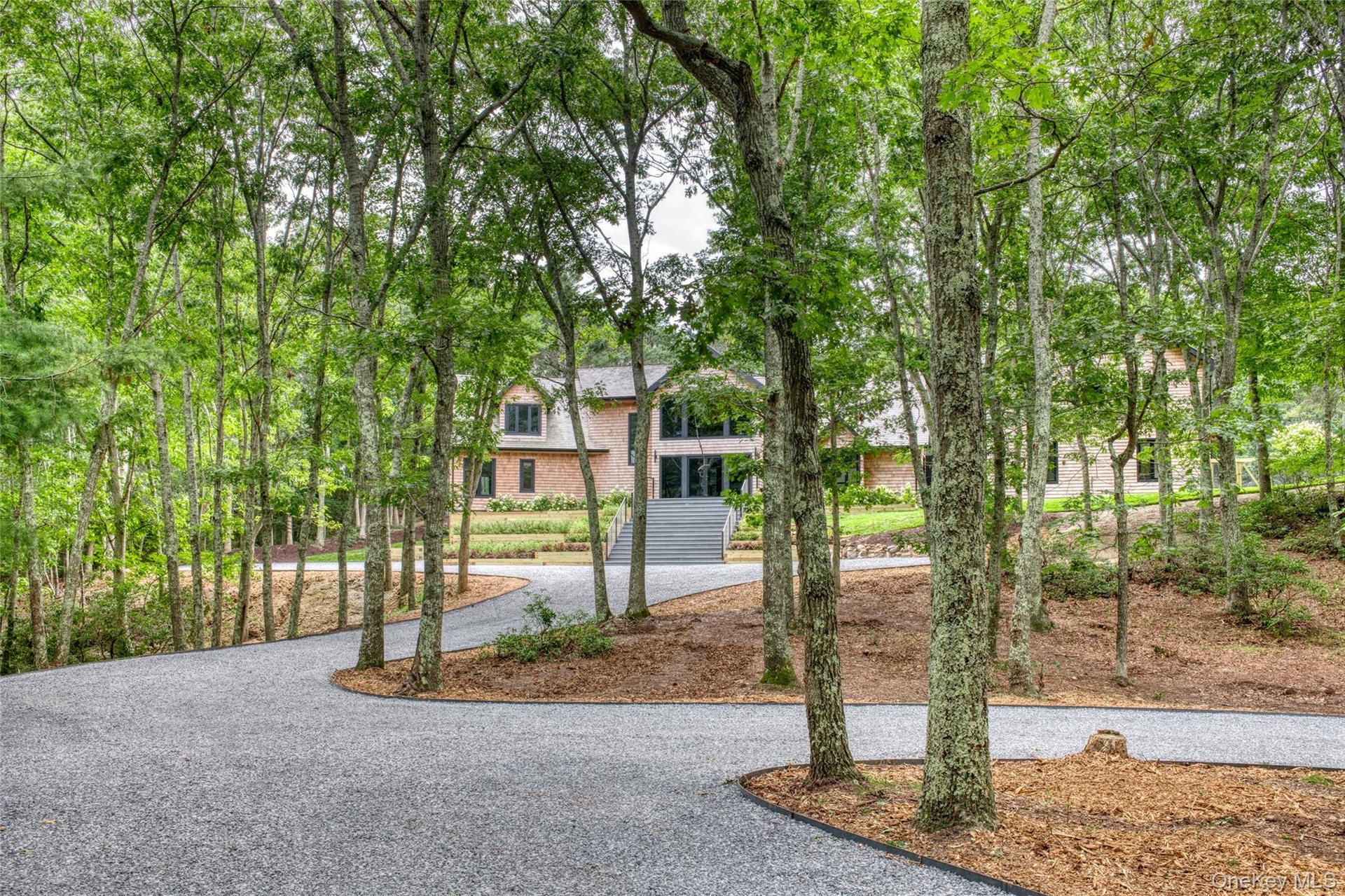 Wooded property with a gravel driveway, mature trees, and a multi-level home featuring gables and wood siding
