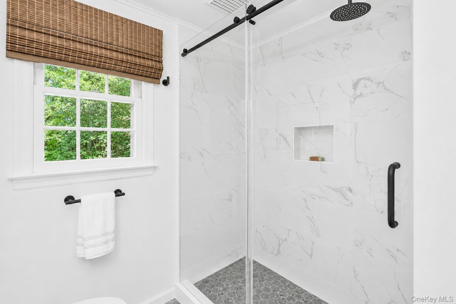 Glass-enclosed shower with a rainfall showerhead, tiled walls, and a built-in shower niche