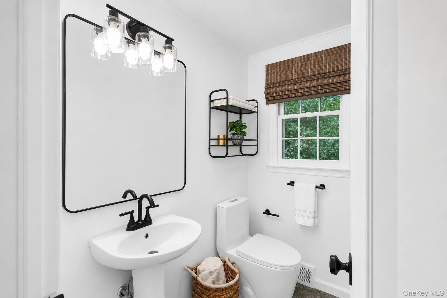 White pedestal sink with matte black faucet, framed mirror, and modern vanity lighting